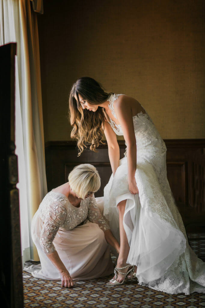Mother of the bride helping her with her shoes near a window. 
