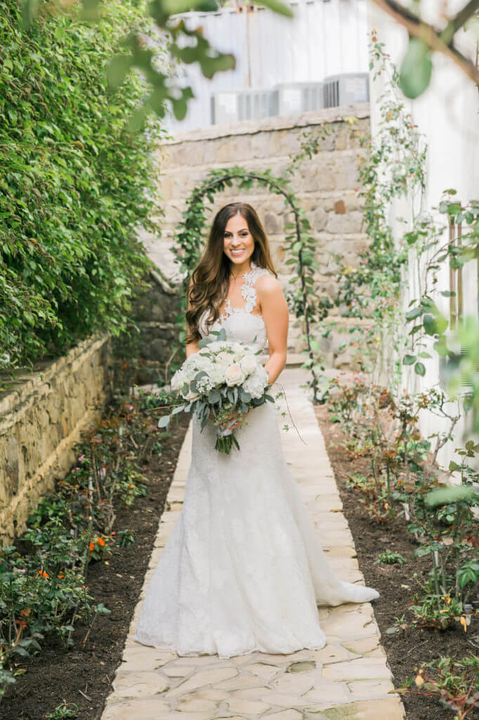 Portrait of a bride wearing a long wedding dress with details embellish holding a bouquet of white roses 