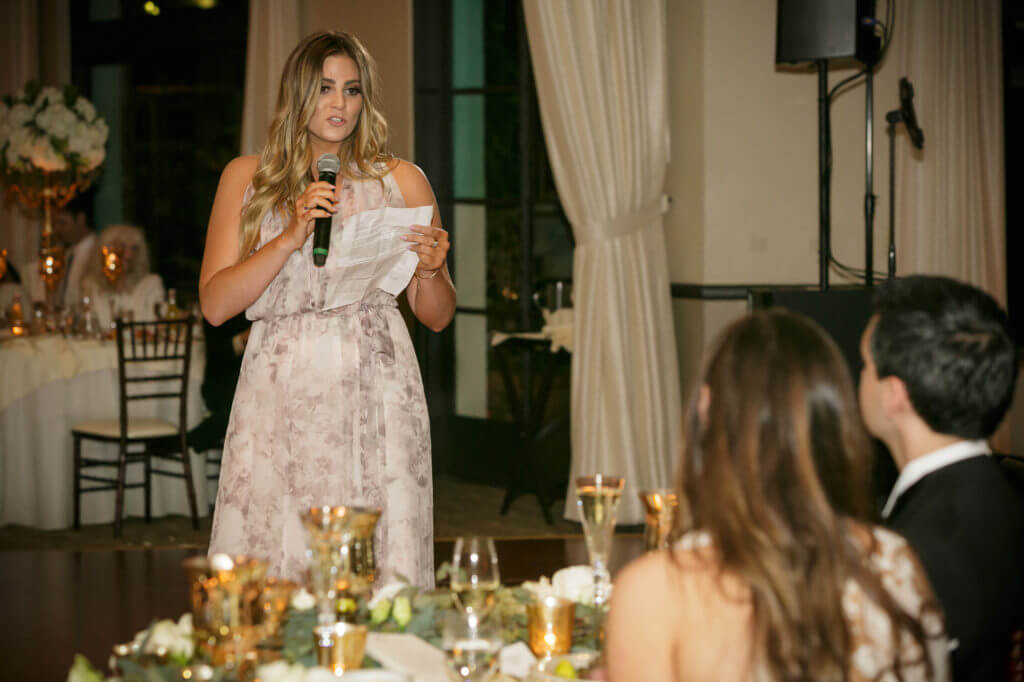 Maid of honor speech during wedding, she is wearing a soft pattern dress with gray and pink. 