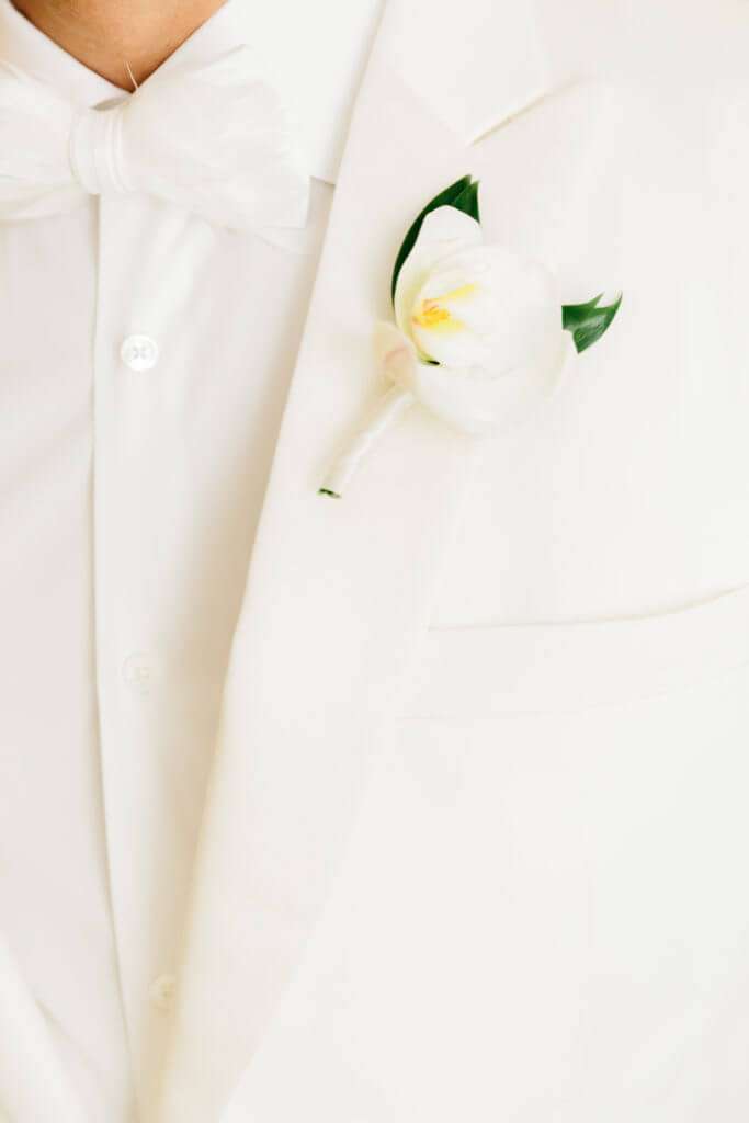 Groom wearing white tux with white orchids