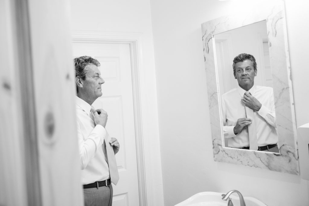 Groom getting ready walking a refelction of himself in the mirror
