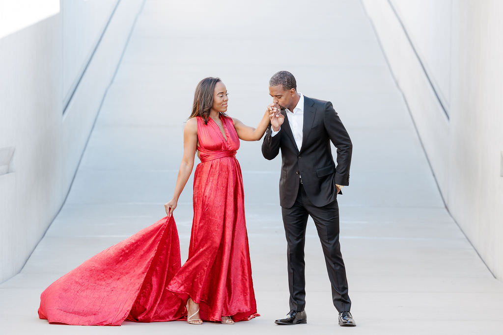 Groom kiising his future bride at MOMA Museum she is wearing a red dress and he is kissing her hand