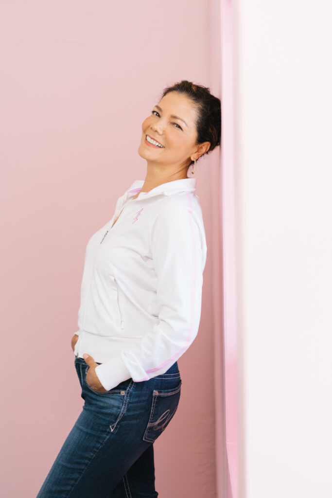 Female wearing a white vintage top leaning on a pink wall 