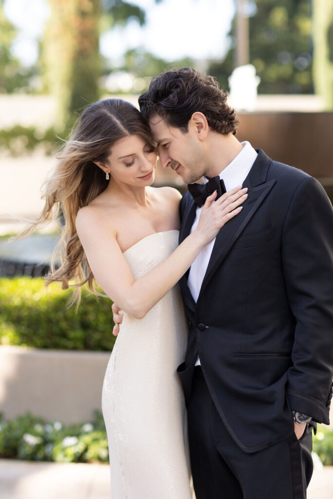 Bride and groom in a romantic outdoor editorial wedding portrait at Waldorf Astoria Beverly Hills, with her diamond ring visible as she holds his tuxedo