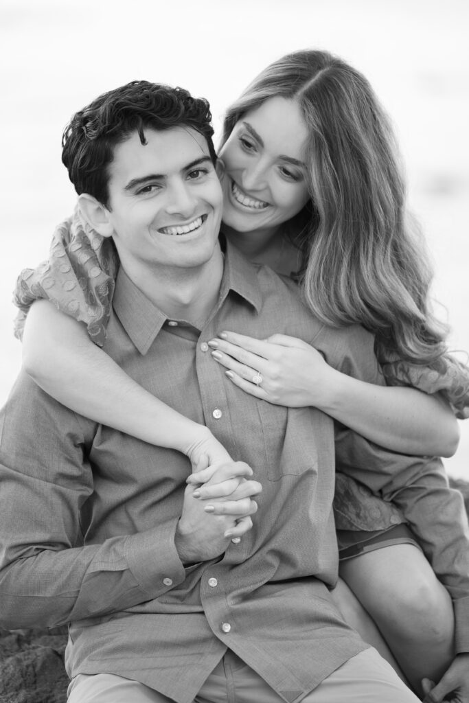 Black-and-white portrait of an engaged couple smiling with the engagement ring visible