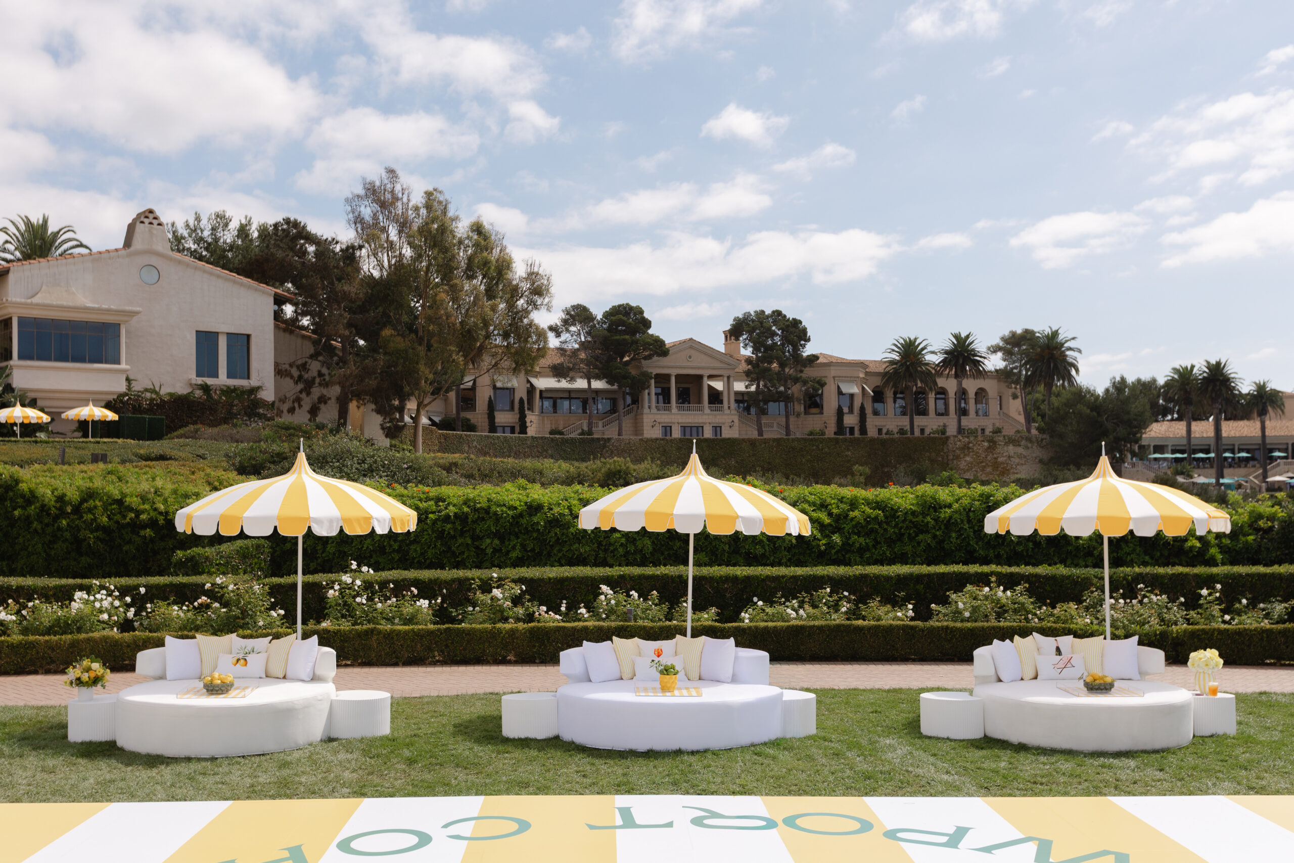 Three white lounge daybeds under yellow striped pagoda umbrellas on the event lawn at The Resort at Pelican Hill in Newport Coast