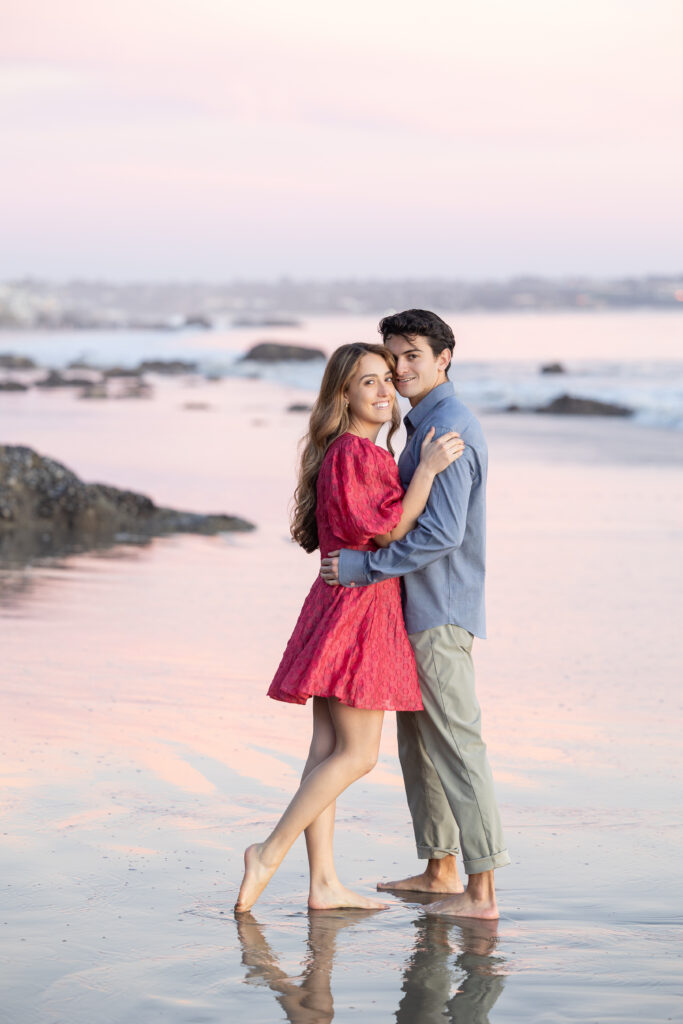 Engaged couple embracing on wet sand during a pastel Malibu sunset.