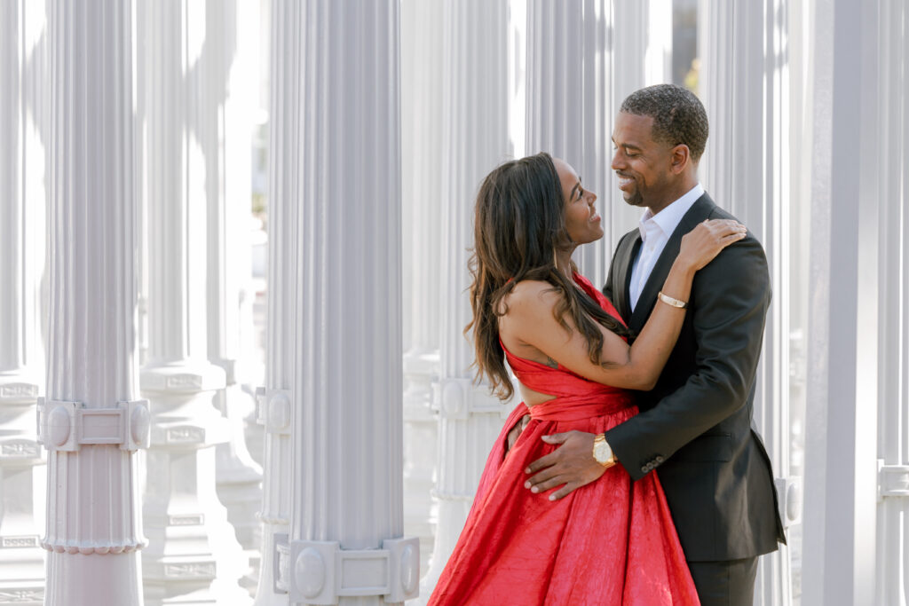 Engaged couple smiling together among the Urban Light lamp posts at LACMA