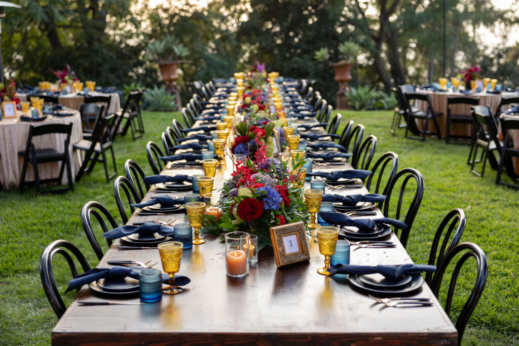 Long reception table with colorful florals, amber glassware, navy details, and candlelight.