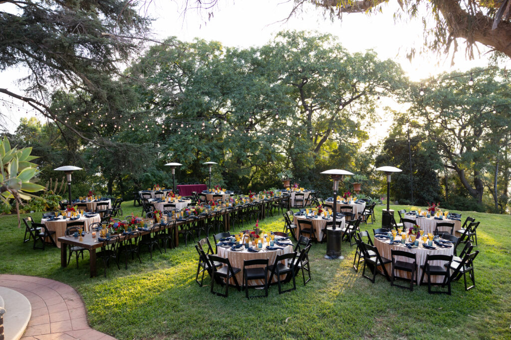 Outdoor garden wedding reception arranged beneath mature trees and string lights by Vanessa Domenesh Events.