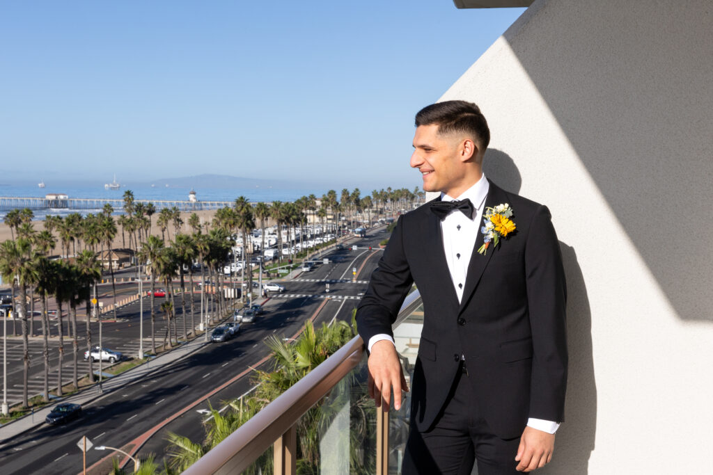 Groom in a black tuxedo overlooking Huntington Beach and the Pacific Ocean from The Waterfront Beach Resort