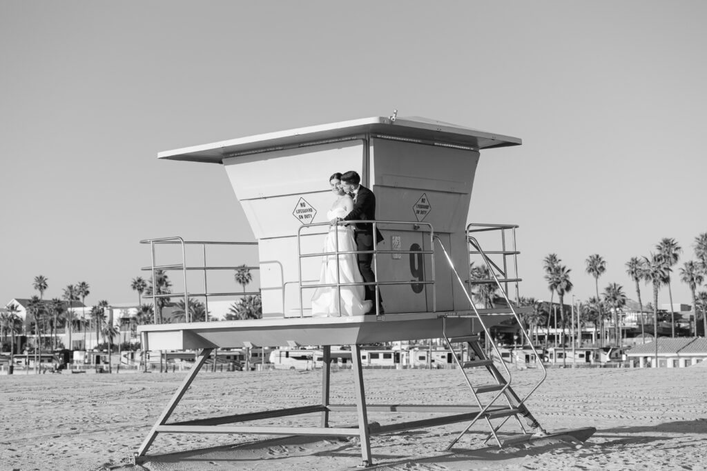Black-and-white wedding portrait of the couple together on a Huntington Beach lifeguard tower